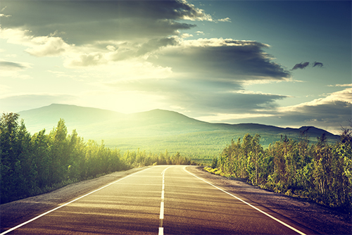 Road through forest into mountains at sunset